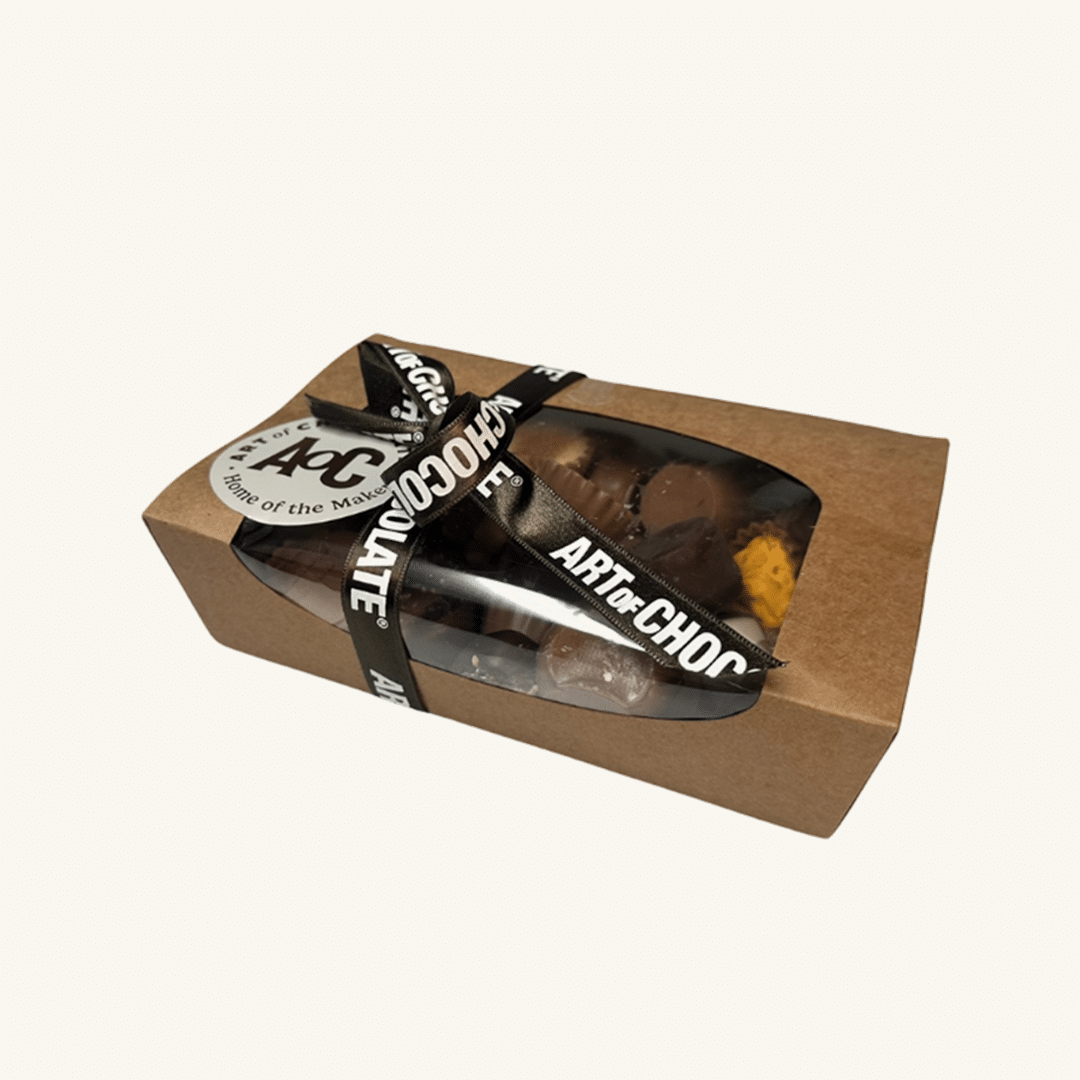Front view of a kraft chocolate ballotin box tied with a black “ART of CHOCOLATE” ribbon and visible assortment inside.